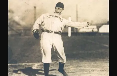 Late 1800s Cincinnati Red Stockings player wearing a white flannel uniform with bright red stockings and the word ‘CINCINNATI’ across the chest