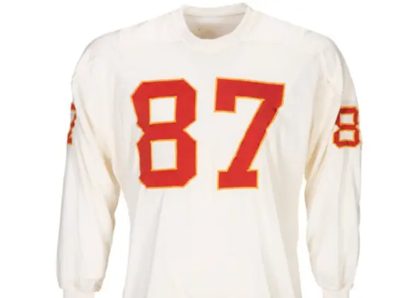 1960–1962 Dallas Texans uniform featuring red jerseys with Columbia Blue numbers and solid red helmets outlined with a white Texas state shape and gold star marking Dallas — the franchise’s original identity before becoming the Kansas City Chiefs