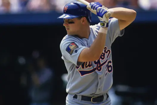1991–1994 New York Mets player wearing a gray road jersey with blue and orange script ‘New York,’ captured mid-swing — representing the transitional ‘Understated Swoosh’ uniform era